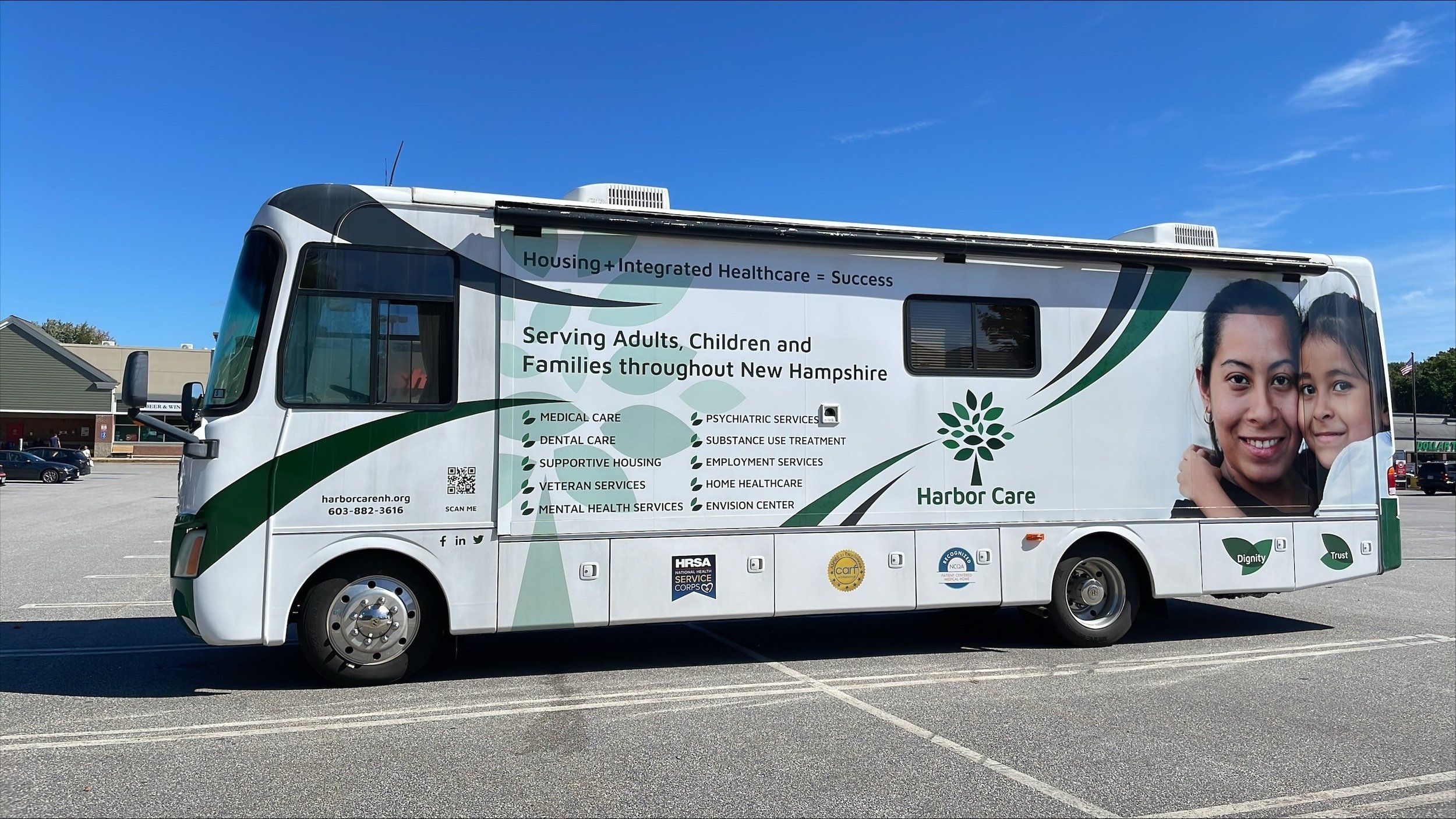 A white Harbor Care mobile unit parked in a lot features images of a woman and a child. The side of the vehicle lists services like healthcare, housing assistance, and mental health services in New Hampshire.