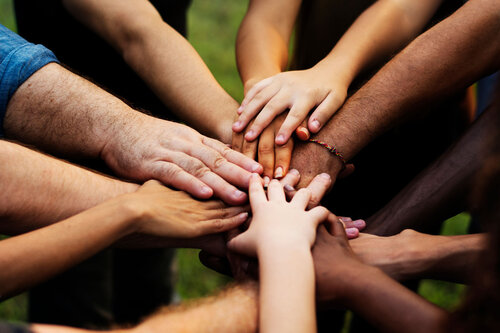 A group of people standing in a circle place their hands together in the center, showing unity and teamwork.