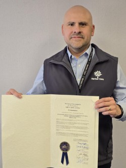 A man wearing a Hartford Care vest holds up an official document with signatures and a seal, standing against a plain background.